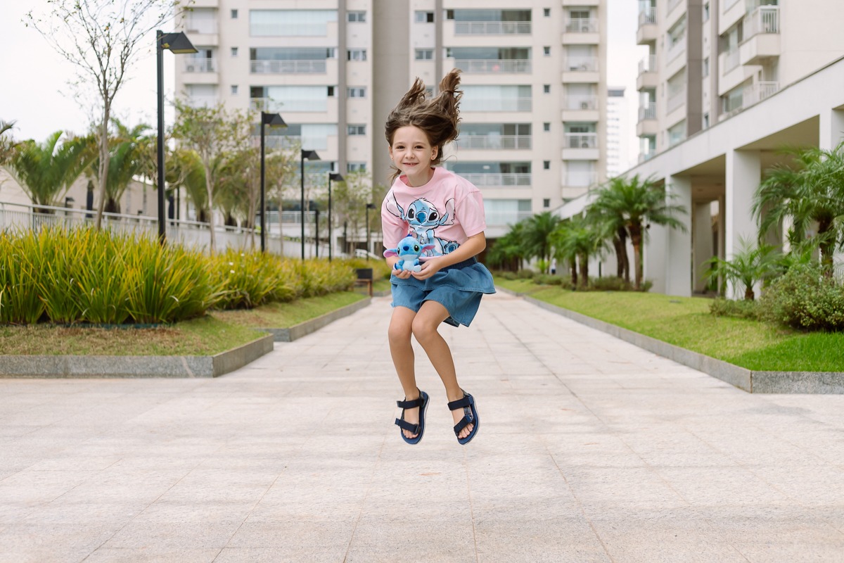 Criança pulando e segurando nas mãos um boneco do Stitch
